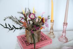 an arrangement of flowers in a vase sitting on top of a book next to a candle