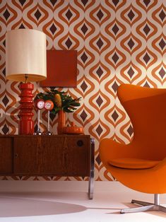 an orange chair sitting next to a lamp on top of a wooden table in front of a wall