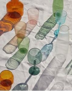 many different colored glasses are lined up on a tablecloth with the shadows from them