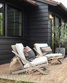 two lounge chairs sitting on top of a wooden deck next to a black building with windows