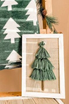 a small christmas tree in a frame on a wooden table next to a green and white blanket