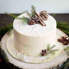 a white frosted cake decorated with pine cones and cinnamon sticks