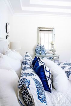 a white couch with blue and white pillows on top of it in front of a mirror