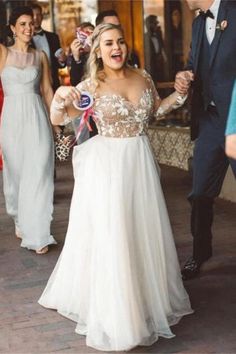 a woman in a white dress is dancing with other people on the sidewalk and smiling