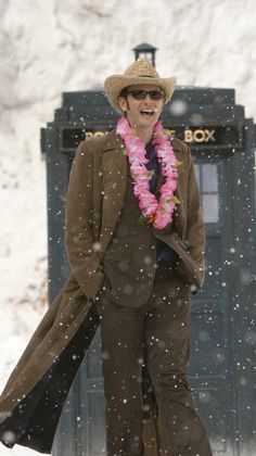 a man in a hat and coat walking through the snow with a pink lei around his neck