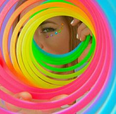 a woman is looking through a circle of neon colored hula hoops with sprinkles on her face