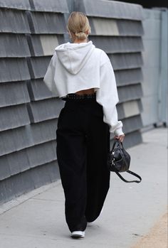 a woman wearing black pants and a white sweater is walking down the street with her handbag