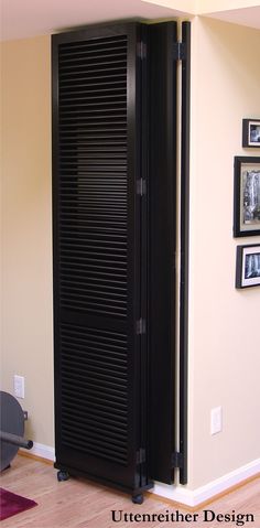 a tall black cabinet sitting in the corner of a room next to a wall with pictures on it