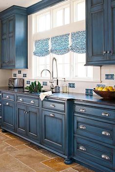 a kitchen with blue cabinets and tile flooring, along with a bowl of fruit on the counter