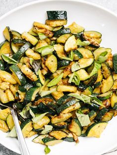 a white plate topped with zucchini and other veggies next to a fork