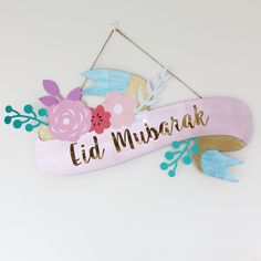 a wooden sign with flowers and leaves hanging from it's side that says, eid mubarak