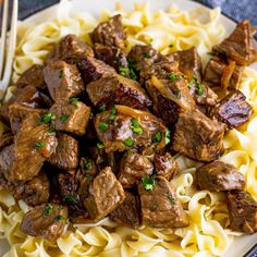 a white plate topped with beef and noodles next to a fork on a tablecloth