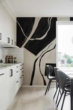 a black and white abstract painting on the wall in a kitchen with chairs around a table