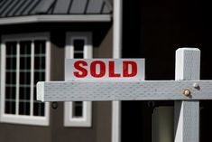 a red sold sign sitting on the side of a white fence in front of a house