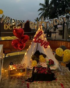 a teepee with balloons and streamers on the ground in front of a happy birthday sign