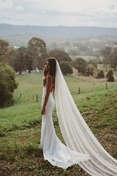 a woman in a wedding dress is standing on a hill with her veil blowing in the wind