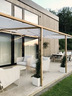 an outdoor patio area with white furniture and wooden posts on the side of the building