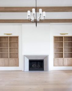 an empty living room with white walls and wooden floors, two open bookcases on either side of the fireplace