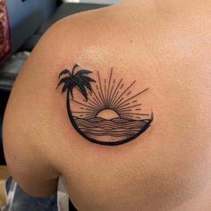 the back of a woman's shoulder with a palm tree and sun tattoo on it