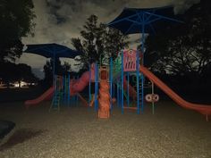 an empty playground at night with blue umbrellas and pink slide in the foreground