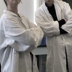 two people wearing lab coats standing next to each other in front of a mirror with their arms crossed