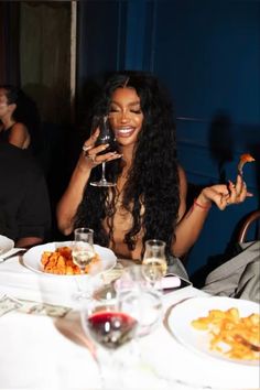 a woman sitting at a table holding a wine glass in her hand and eating food