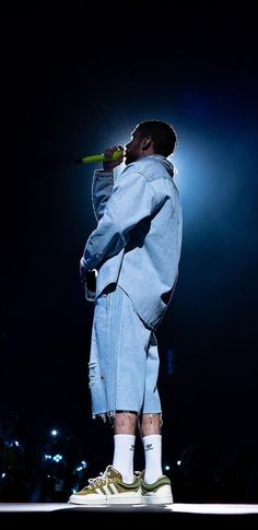 a man standing on top of a stage with his hands in his pockets while holding a microphone