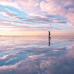 a person walking across a large body of water under a cloudy blue and pink sky