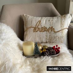 a candle and some christmas decorations sit on a white fur covered chair next to a pillow