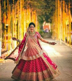 a woman in a red and gold lehenga poses for the camera with her arms outstretched