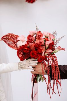 two hands holding a bouquet of red and pink flowers