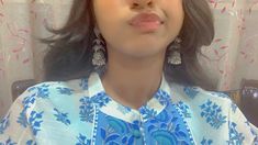 a woman in a blue and white shirt with large earrings on her head looking at the camera