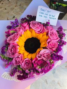 a bouquet of pink roses and yellow sunflowers with a note attached to it