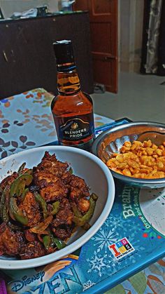 a table topped with two bowls filled with food and a bottle of alcohol next to it