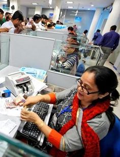 a woman sitting at a desk in an office with people working on computers and papers