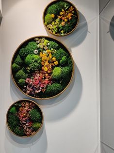 three bowls filled with broccoli and other vegetables on top of a white surface