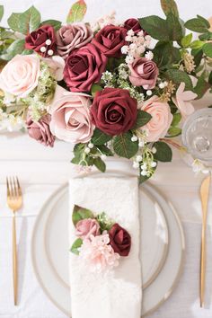 the table is set with white plates, silverware and pink flowers in vases