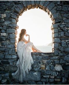 a woman sitting on top of a stone wall