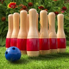 several wooden bowling pins lined up next to a blue ball on the grass with flowers in the background