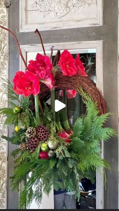 a wreath with red flowers and greenery hanging from the front door to be used as a decoration