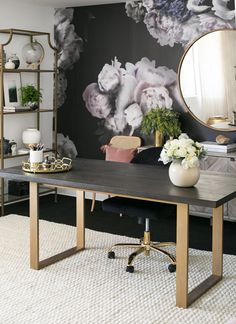 a desk with flowers on it and a mirror in the corner next to some chairs