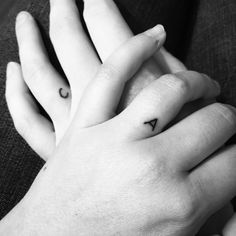 two hands holding each other with small tattoos on their fingers, one has a heart and the other has an arrow