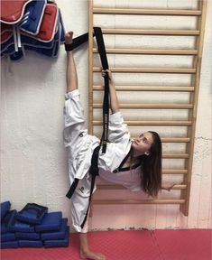 a woman in white shirt and black belt doing a handstand on the floor