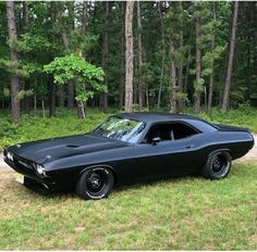 an old black muscle car parked in the grass