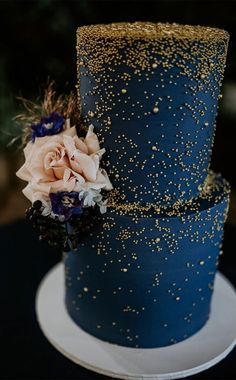 two tiered blue wedding cake with gold sprinkles and flowers on top