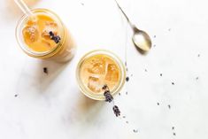 two glasses filled with iced tea and lavender sprigs next to spoons on a marble surface