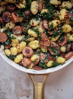 a pan filled with sausage, potatoes and spinach on top of a countertop