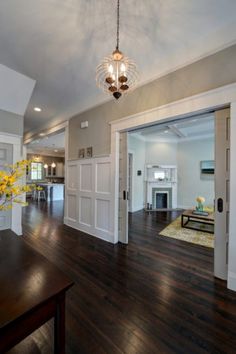 an empty living room with hard wood flooring and white walls, chandelier