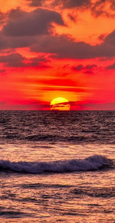 the sun is setting over the ocean with waves in front of it and clouds in the sky