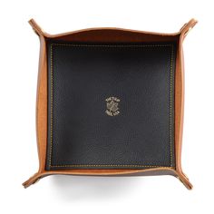 a black and brown leather tray with a gold emblem on the front, sitting on a white surface